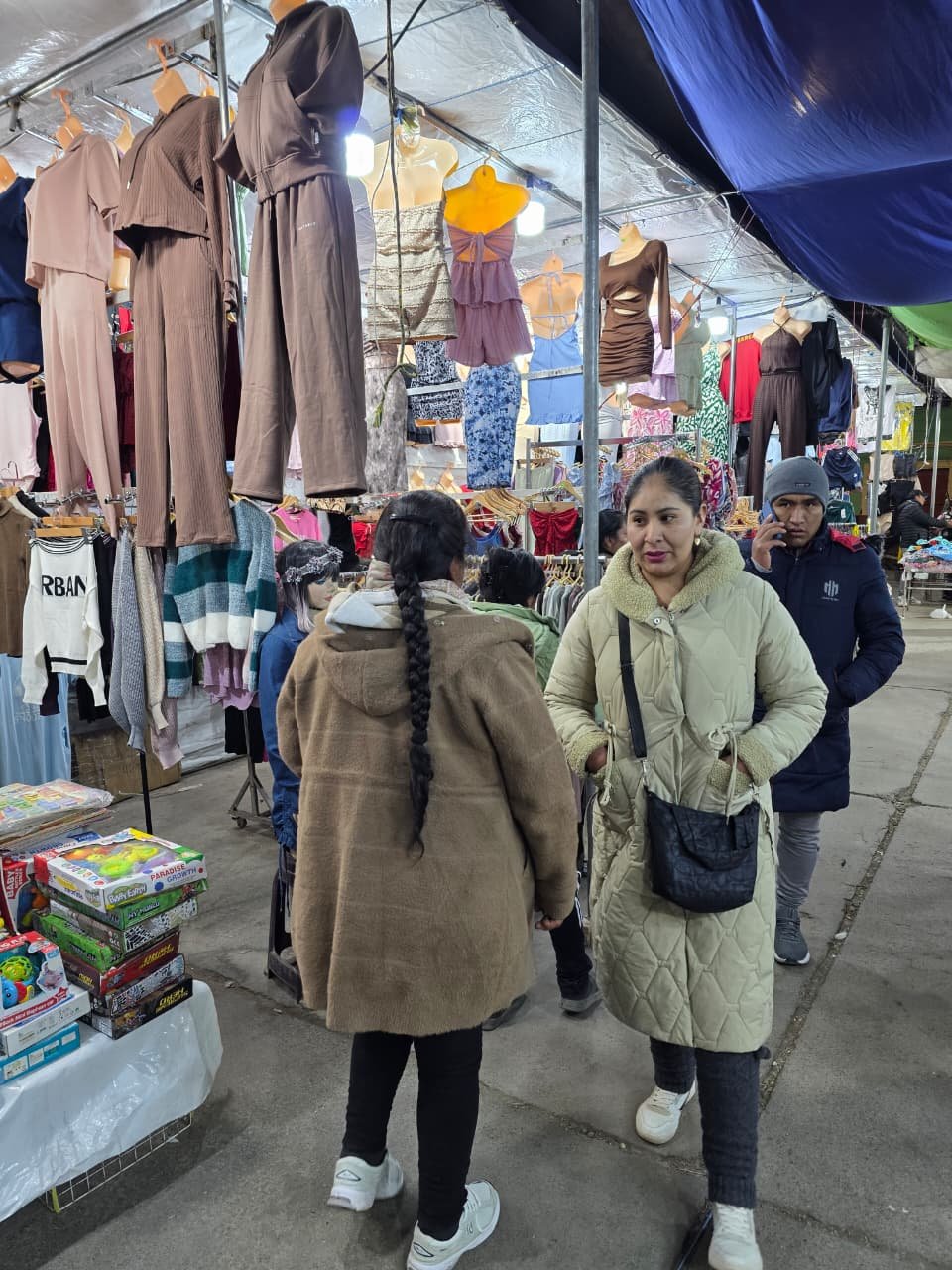 Pasillo de una feria de Gran Feria de Gamarra con stands de ropa colgada y visitantes recorriendo los puestos.