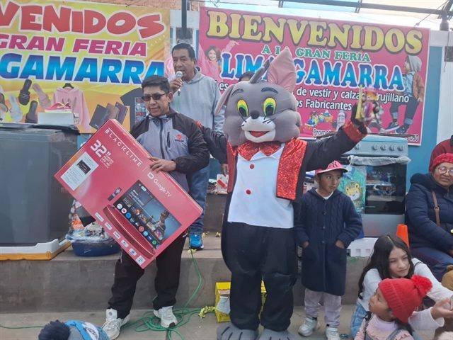 Entrega de un televisor de 32 pulgadas en el escenario de la feria, junto a la mascota y el público.