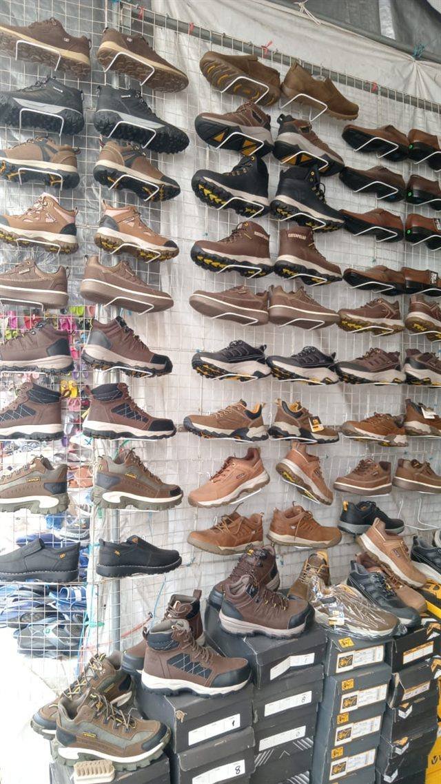 Stand de calzado con zapatillas y botines de trabajo exhibidos en una malla y cajas apiladas.