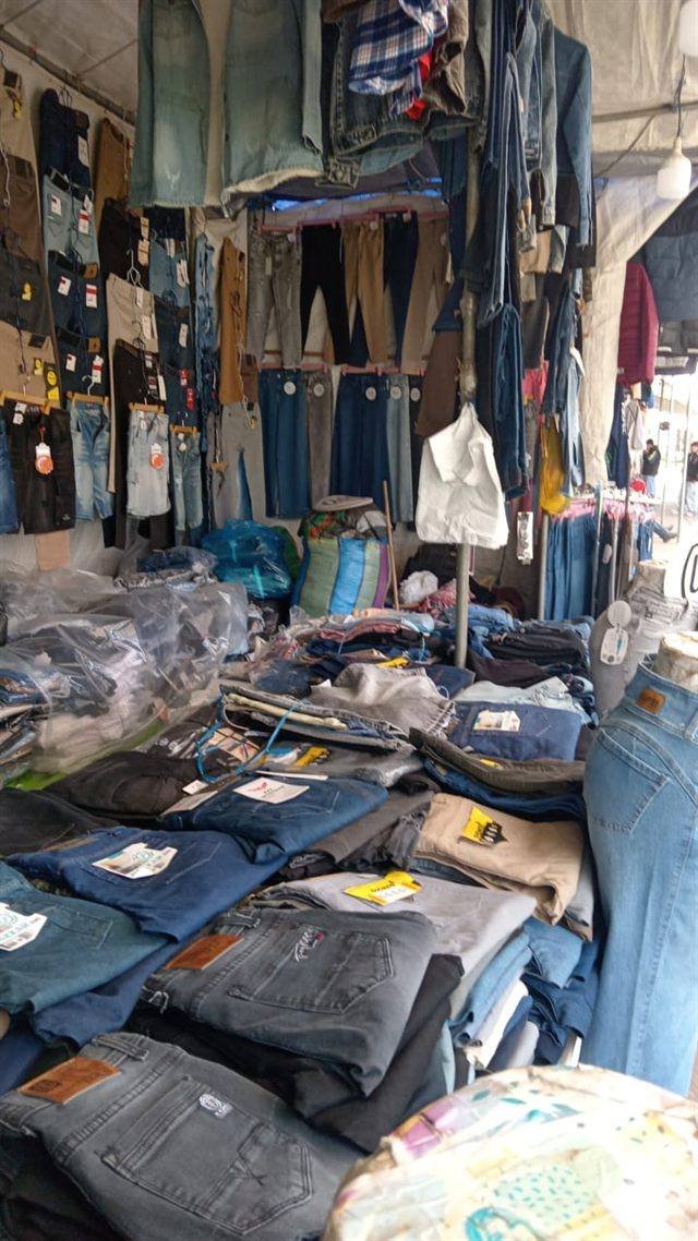 Stand de jeans con pantalones doblados sobre mesas y prendas de mezclilla colgadas al fondo.