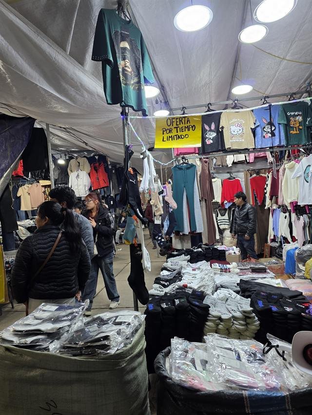Stand de medias y ropa con mesas llenas de calcetines, polos y prendas de abrigo colgadas.
