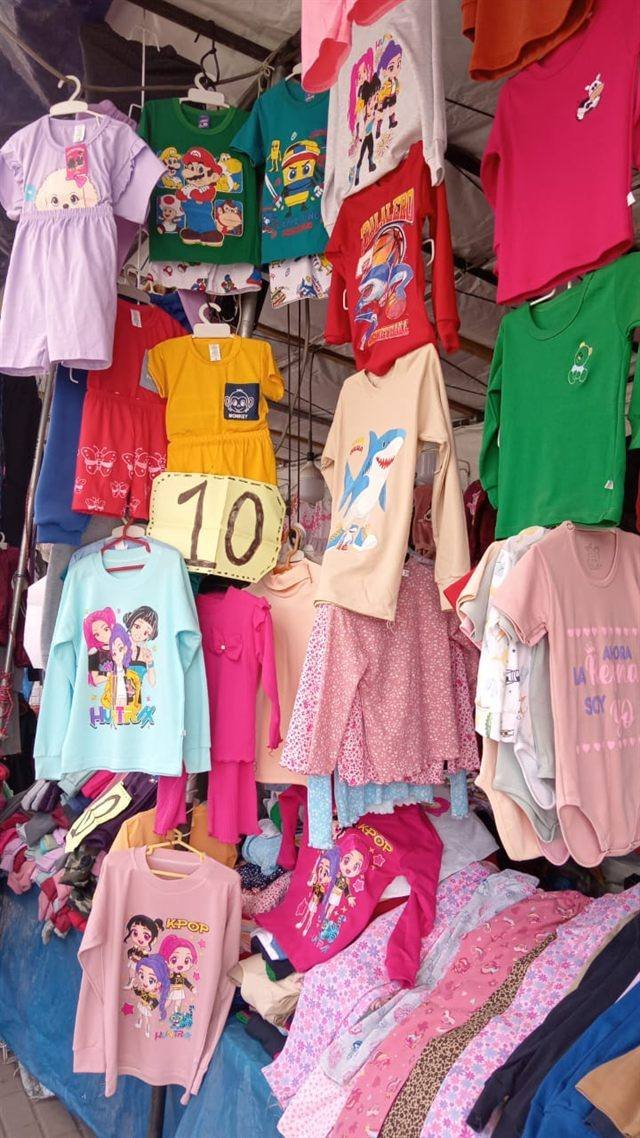 Stand de ropa infantil con polos, conjuntos y pijamas de colores colgados y apilados.