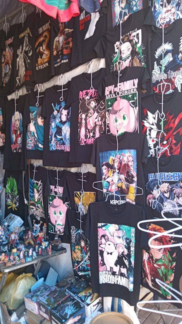 Stand de polos negros con estampados de anime, bandas y personajes, colgados en perchas.