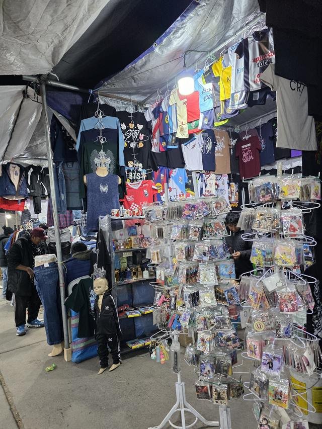 Stand de ropa deportiva con camisetas de fútbol colgadas y accesorios en exhibidores giratorios.
